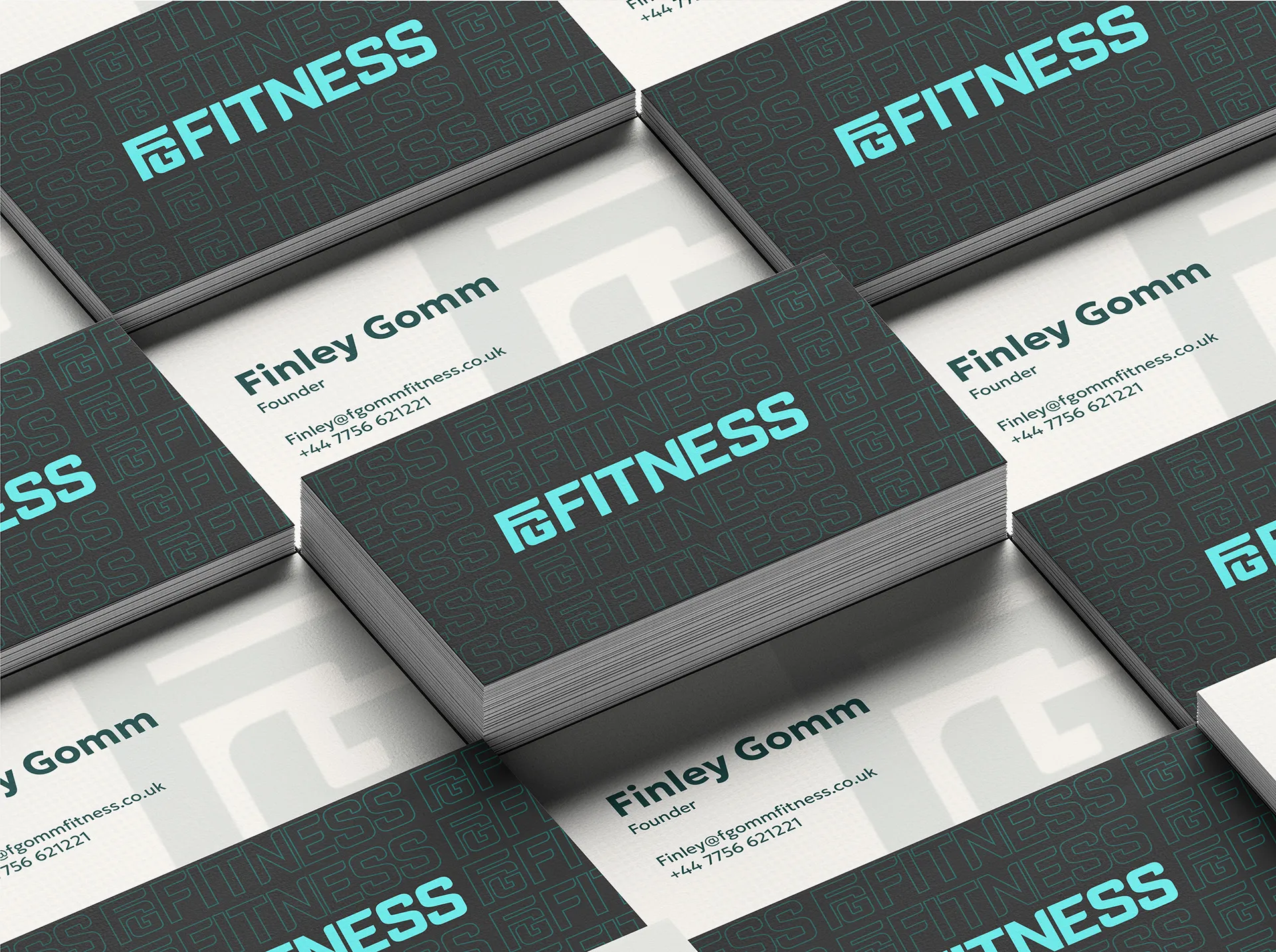 A stack of business cards for FG Fitness, featuring the company's logo and contact information. The cards are arranged in a staggered pattern, with some facing up and others down, showcasing the design and layout of the card.