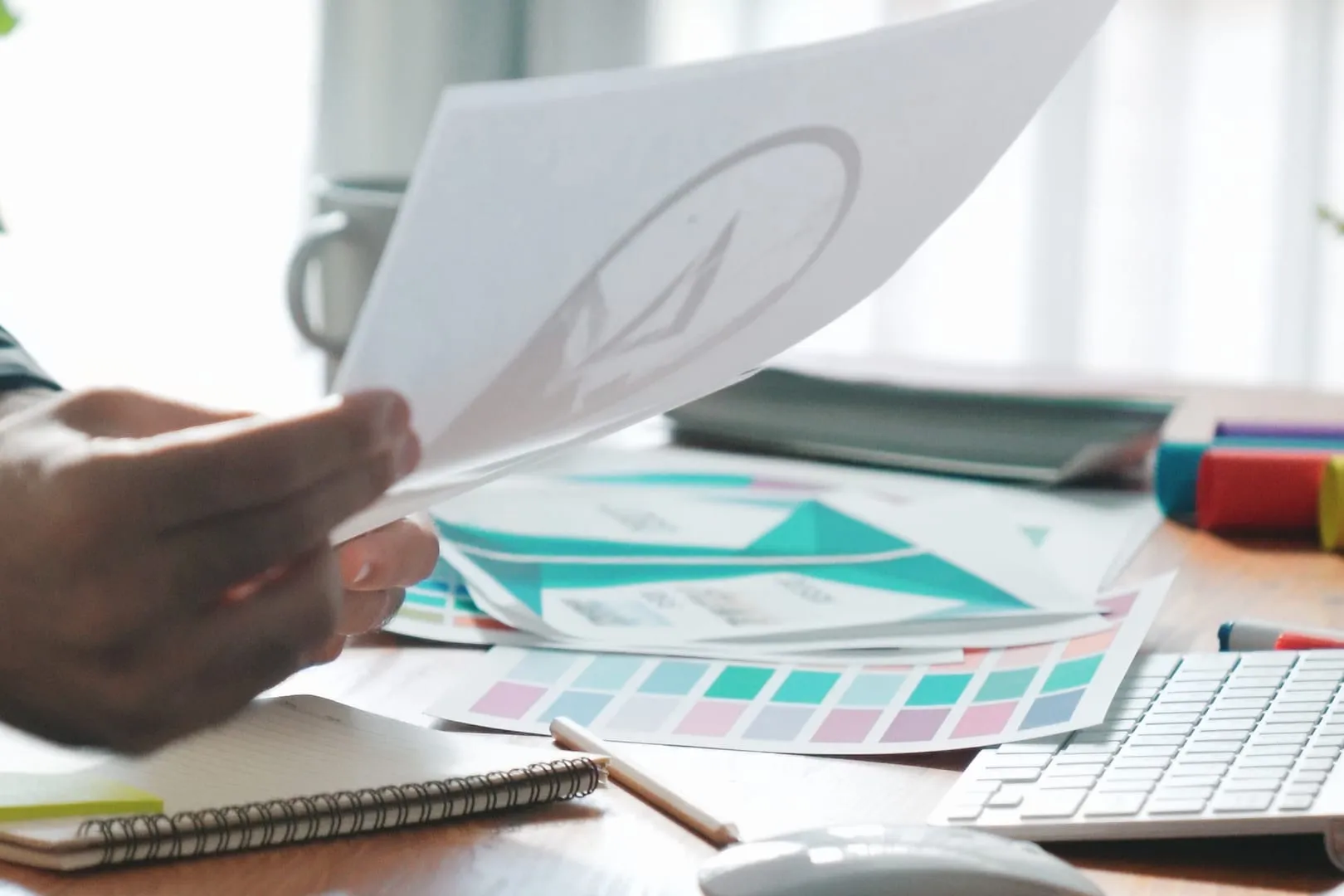 Designer reviewing a printed logo mark beside colour palettes on a bright studio desk