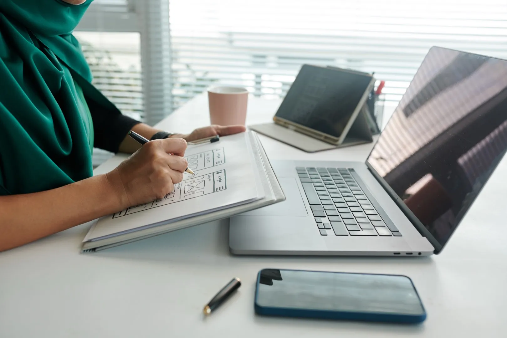 UI designer sketching website and mobile interface layouts on paper at a desk