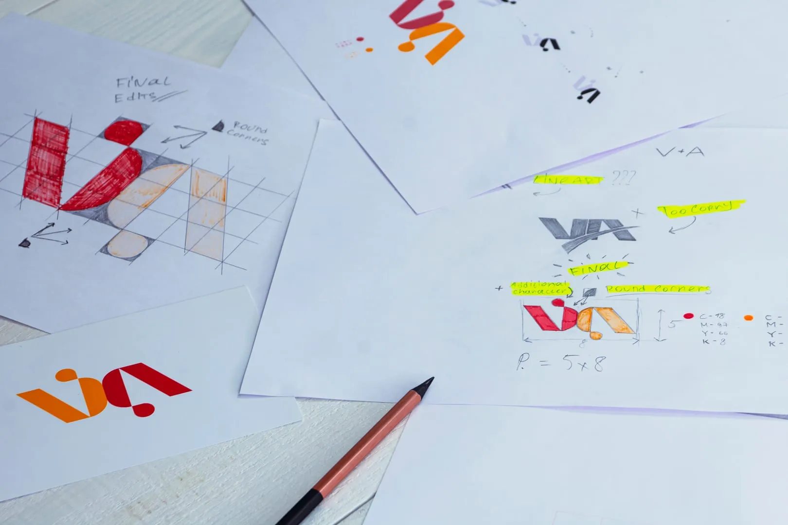 Logo sketch sheets with geometric mark iterations, grid notes and markers on a studio desk