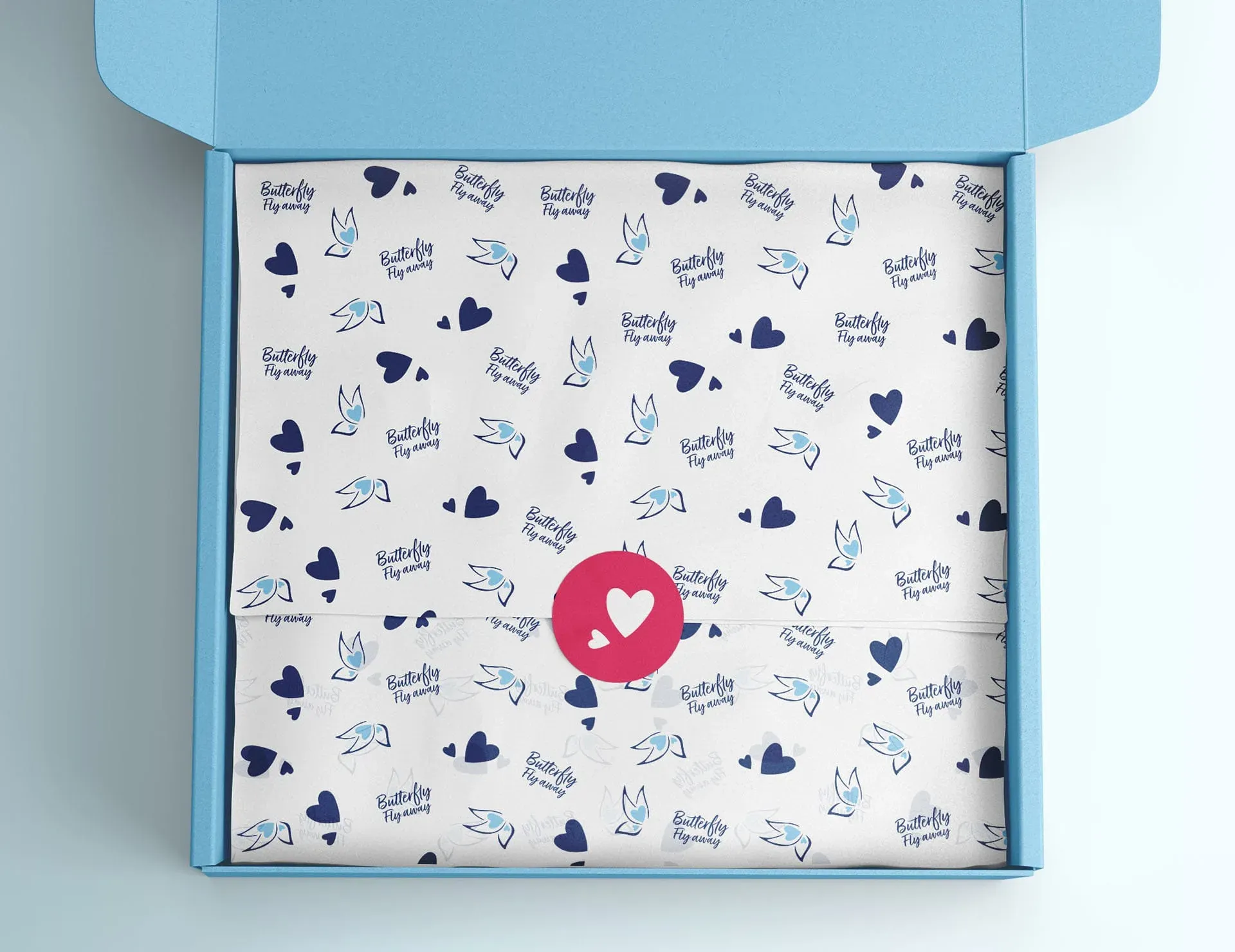 A light blue cardboard box with a white interior, featuring a repeating pattern of navy hearts and blue and light blue birds, with the words "Butterfly Fly Away" in navy and blue. The box is open, with the lid propped up, and a pink circle